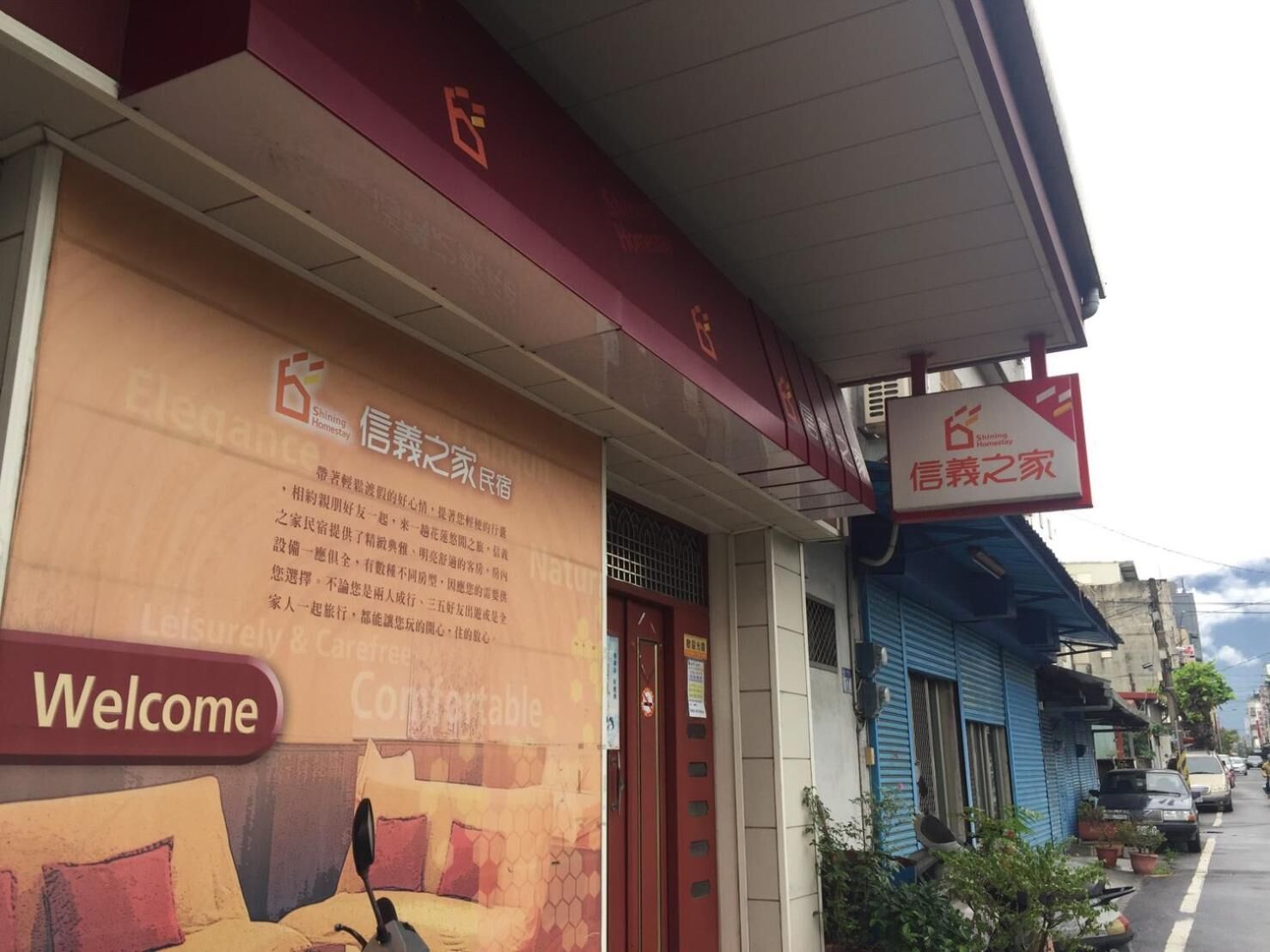 A hotel exterior with a large welcome sign, a signboard with Chinese text, and a blue awning.