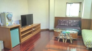 Une chambre d’hôtel compacte comprenant un bureau en bois, un téléviseur à écran plat, une table basse en verre, un canapé et un lit.