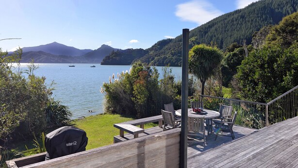 A deck with outdoor furniture overlooking a lake, surrounded by greenery and hills. - Ngaire's Haven - Mahau Sound Holiday Home (Mahau Sound)