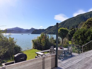 Une terrasse dotée de mobilier d’extérieur, offrant une vue sur un lac et entourée de verdure et de collines.