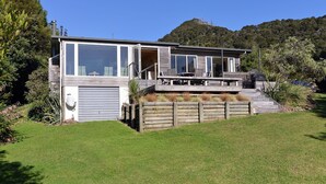 A modern house with a large garage, a deck with outdoor furniture, and a lush garden. - Ngaire's Haven - Mahau Sound Holiday Home (Mahau Sound)