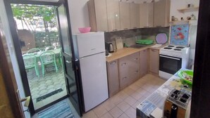 Cocina compacta con refrigerador, estufa y lavamanos. Se observan gabinetes y un pequeño comedor.