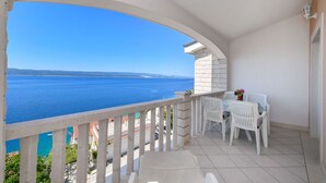 A balcony with a view of the sea, white furniture, and a tiled floor.