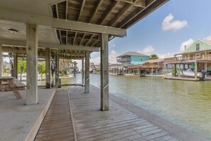 A wooden pier with a covered seating area and a view of houses along a calm waterway.