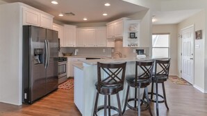 Una cocina moderna con armarios blancos, un refrigerador de acero inoxidable, una isla central con taburetes de bar e iluminación empotrada en el techo.