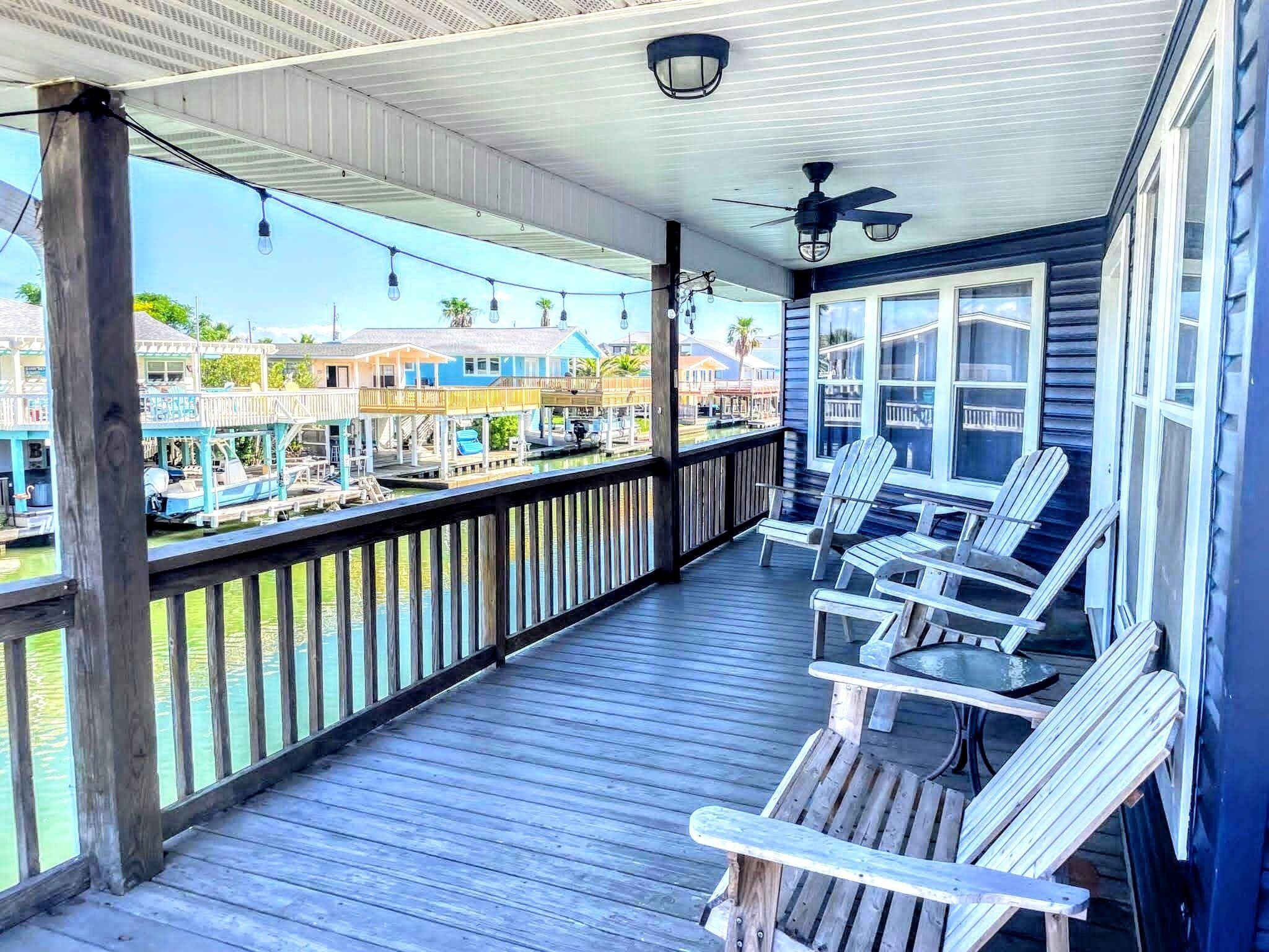 A wooden deck with Adirondack chairs, a railing, and a view of a marina with boats.