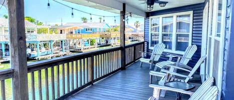 A wooden deck with Adirondack chairs, a railing, and a view of a marina with boats.