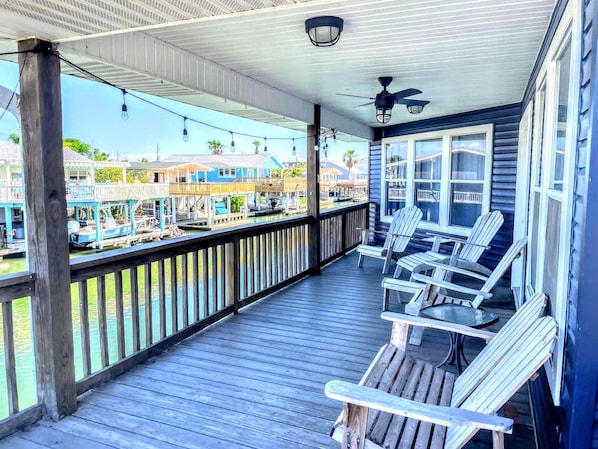 A wooden deck with Adirondack chairs, a railing, and a view of a marina with boats.