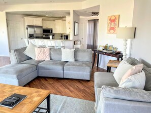 A modern living room with a grey sectional sofa, a wooden coffee table, and a dining area with a small table and chairs.