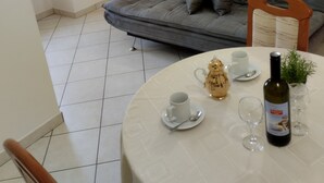 Un salón con un sofá gris, una mesa de comedor con una botella de vino, una taza de café y una pequeña planta.