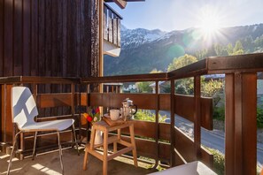 Un balcon avec une chaise en bois, une petite table en bois sur laquelle se trouve une cafetière, et une vue sur des montagnes enneigées.