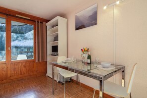 Un coin repas avec une table en verre, des chaises blanches, un buffet blanc et un tableau au mur.