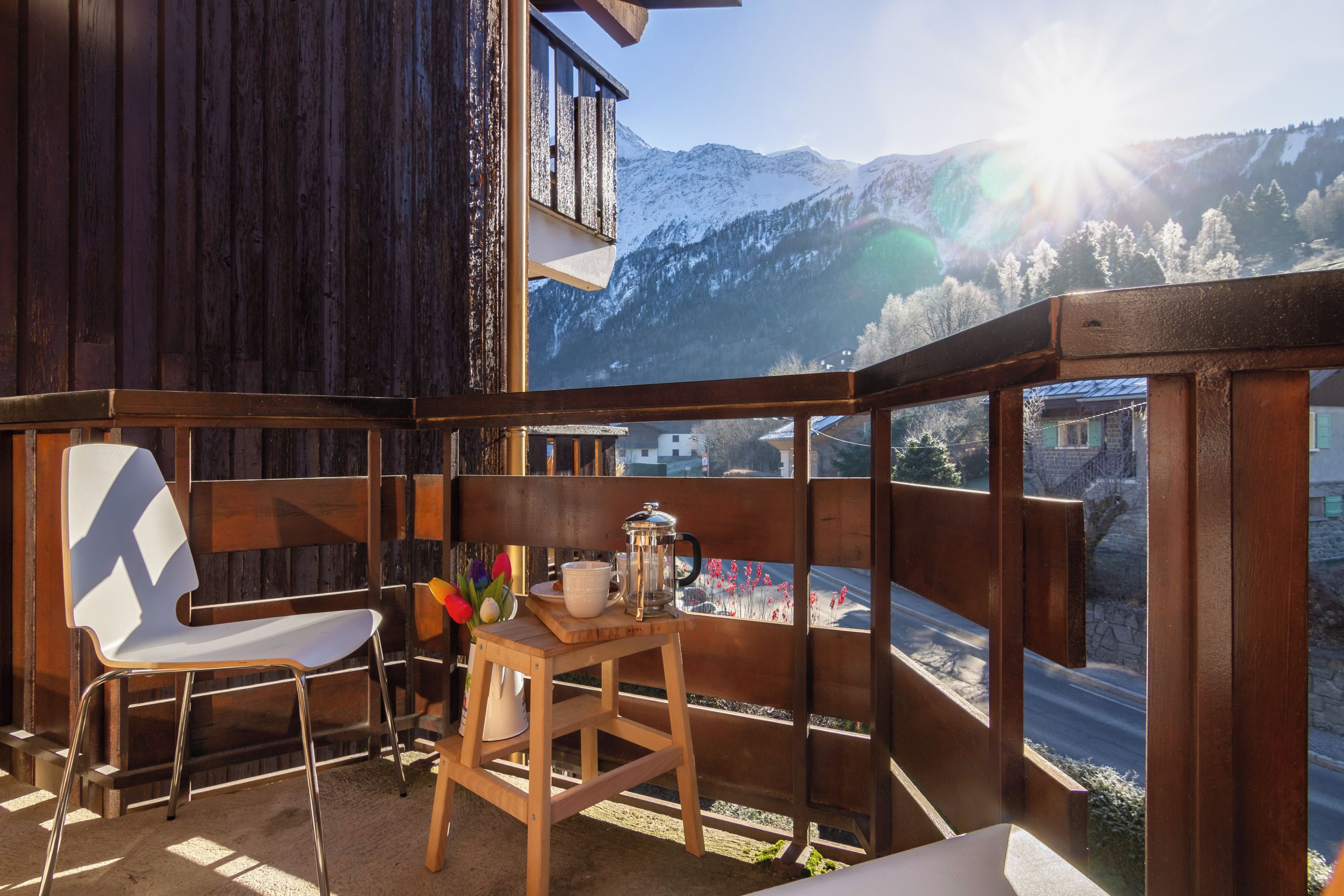 A balcony with a wooden chair and a small table, overlooking a snowy mountain landscape.