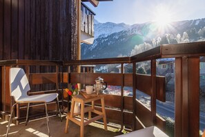 A balcony with a wooden chair and a small table, overlooking a snowy mountain landscape. - Le Prarion 24A Ski in/Ski out at Les Houches (Sleeps 4), Les Houches (Chamonix), France (Les Houches (Chamonix))