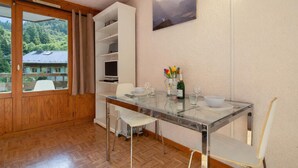 Un comedor con mesa de vidrio, sillas blancas, un armario blanco y un cuadro en la pared.