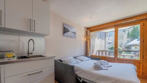 Un dormitorio con cama, ventana, lavamanos y una pequeña kitchenette.