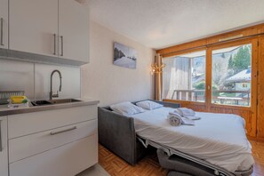 Un dormitorio con cama, ventana, lavamanos y una pequeña kitchenette.