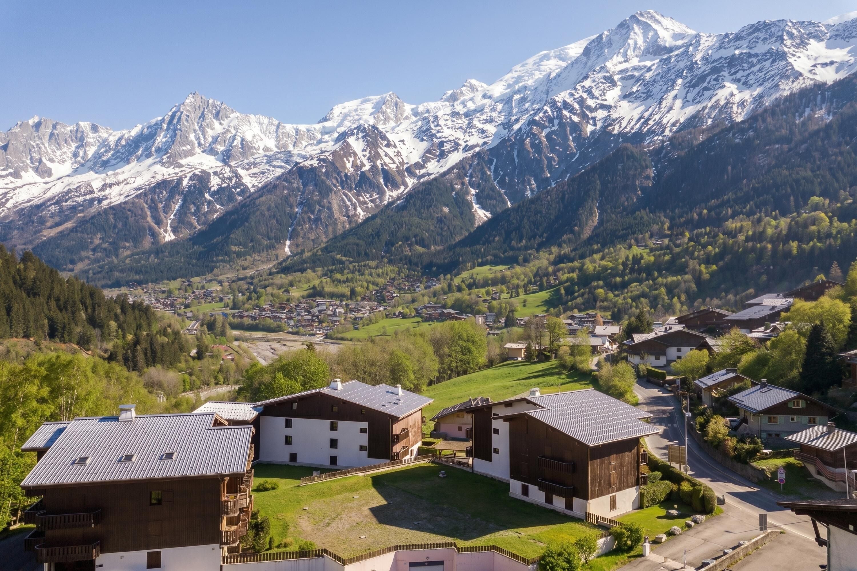 A mountainous village with traditional wooden houses, a clear sky, and snow-capped peaks in the background.