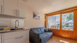 Una cocina moderna con armarios blancos, un sofá gris y un ventanal con vistas a casas.