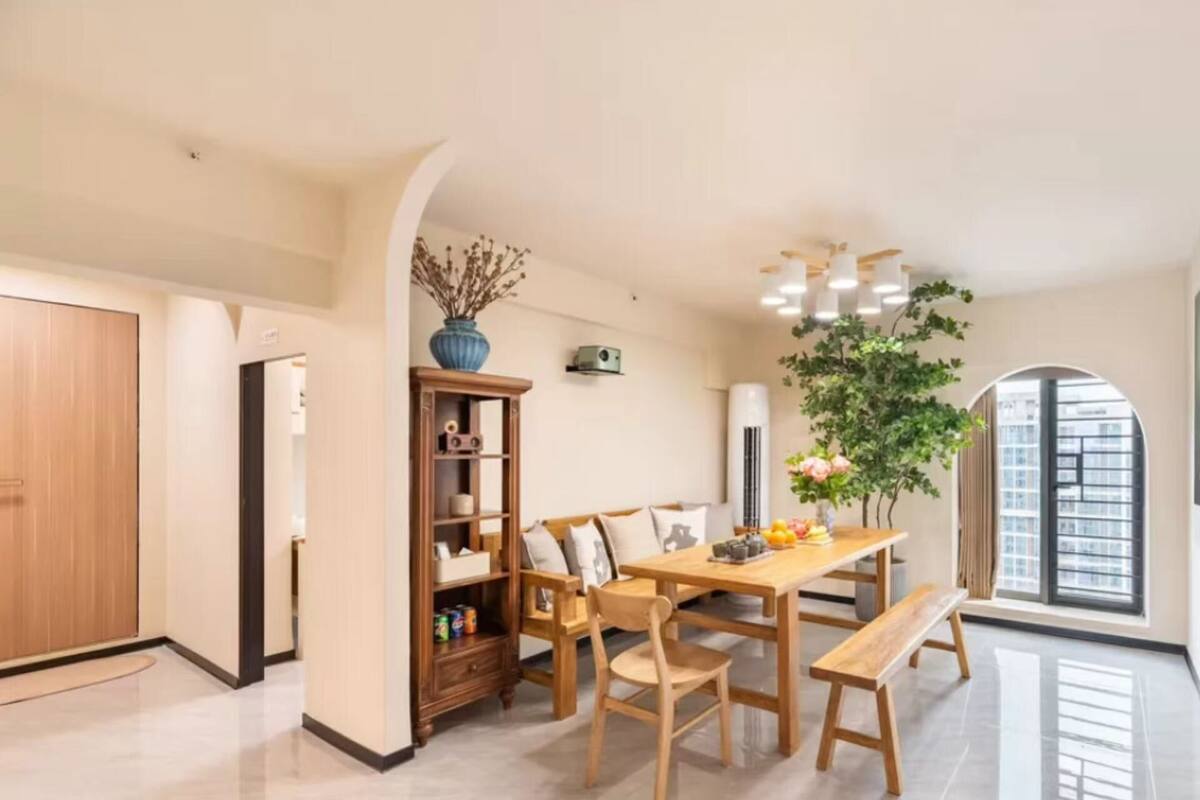 A spacious dining area with a wooden table and chairs, a large potted plant, and a modern ceiling light fixture.