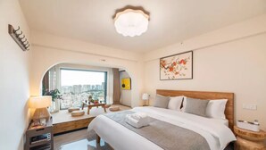 Ein Hotelzimmer mit einem großen Bett, einem Schreibtisch mit Lampe, Blick auf die Stadt durch ein Fenster und einer Deckenleuchte.