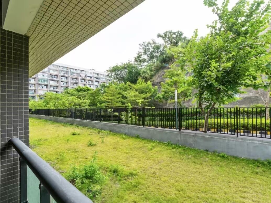 A balcony with a view of a grassy area, a black metal fence, and a building in the background.