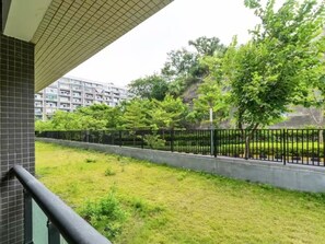 Un balcon donnant sur un espace verdoyant, une clôture en métal noir et un bâtiment en arrière-plan.