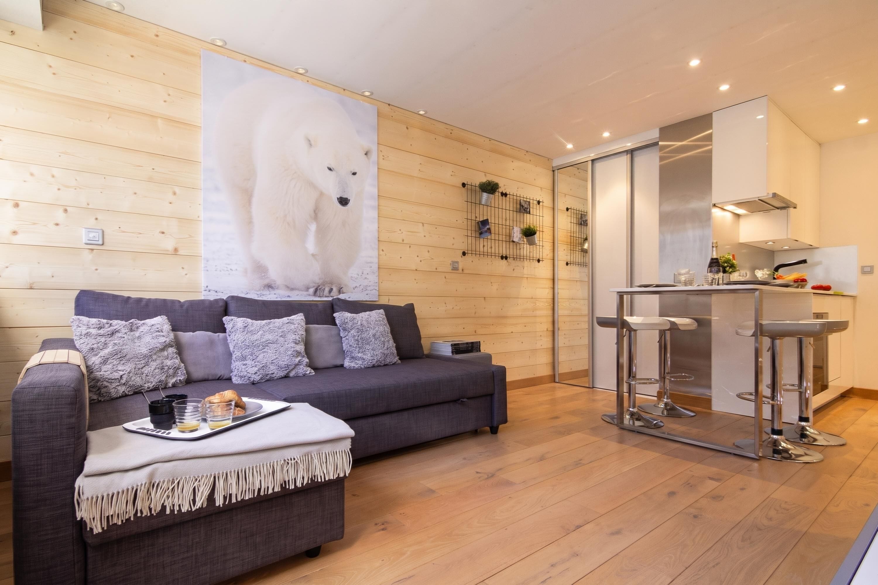 A modern living room with a grey sofa, a coffee table with a tray of croissants, and a large polar bear poster on the wall.