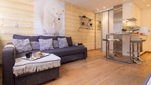 A modern living room with a grey sofa, a coffee table with a tray of croissants, and a large polar bear poster on the wall. - Apt Le Concordia 4 Chic 2BR in Chamonix Centre | Ski, Chamonix, France (Chamonix)