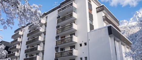 Un immeuble résidentiel à plusieurs étages, doté de balcons, entouré d’arbres couverts de neige.