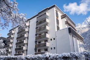 Un edificio residenziale a più piani con balconi, circondato da alberi innevati.