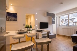 Une cuisine moderne avec un coin repas, des tabourets de bar, un téléviseur fixé au mur et une fenêtre donnant sur un paysage enneigé.