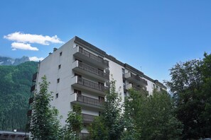 Un edificio de varios pisos con balcones, rodeado de árboles y montañas.