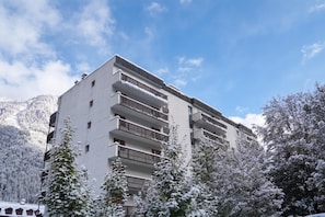 Un immeuble à plusieurs étages doté de balcons, entouré d’arbres et de montagnes couverts de neige.