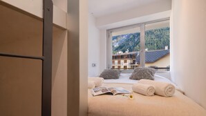 A bedroom with a bed, pillows, a book, and a window with a mountain view. - Apt Le Concordia 4 Chic 2BR in Chamonix Centre | Ski, Chamonix, France (Chamonix)