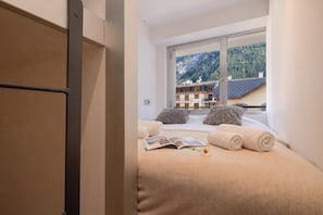 Una camera da letto con un letto, cuscini, un libro e una finestra vista montagna.