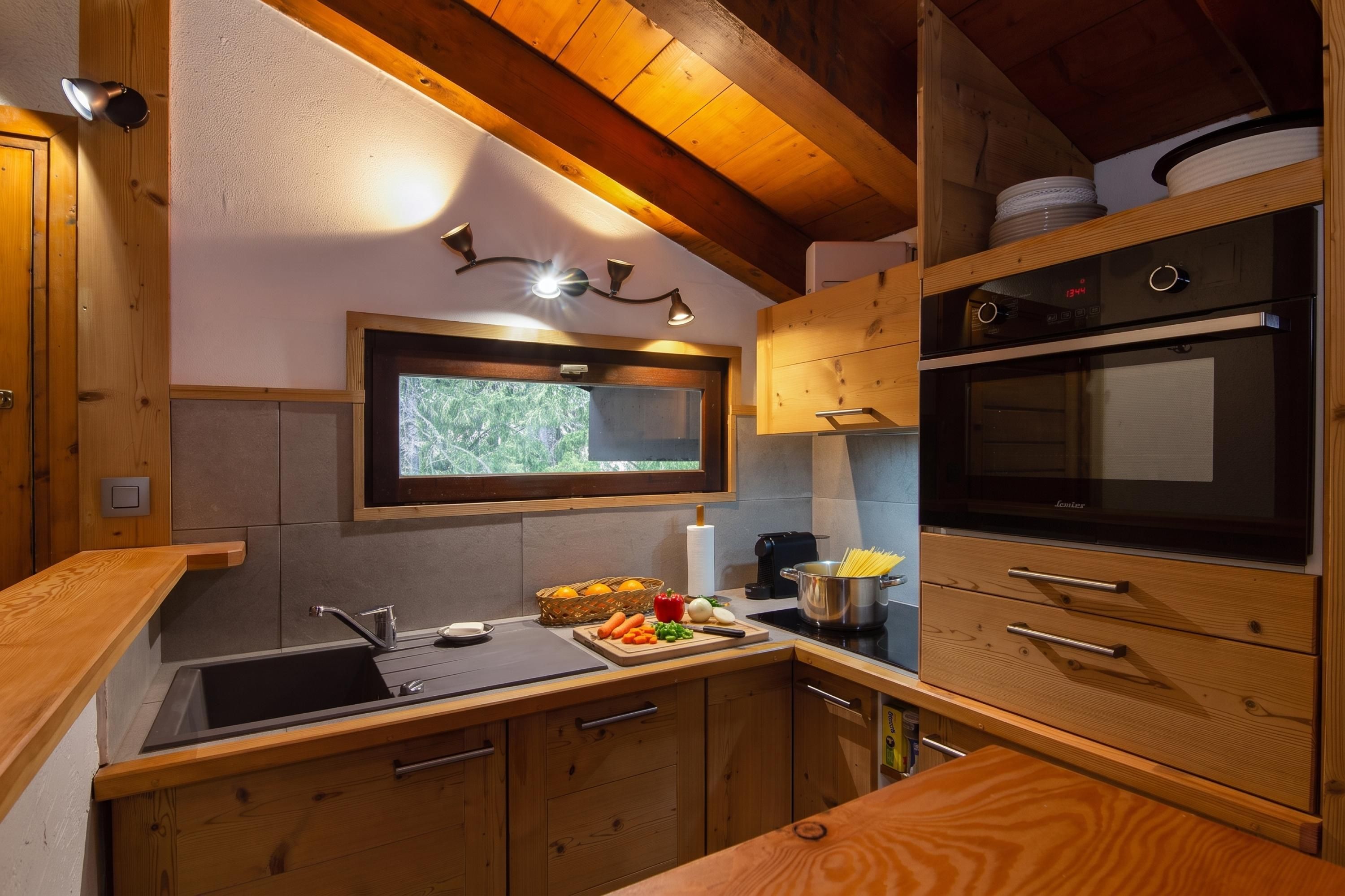 Une cuisine de taille réduite, avec des meubles en bois, un four encastré et une fenêtre au-dessus de l’évier.
