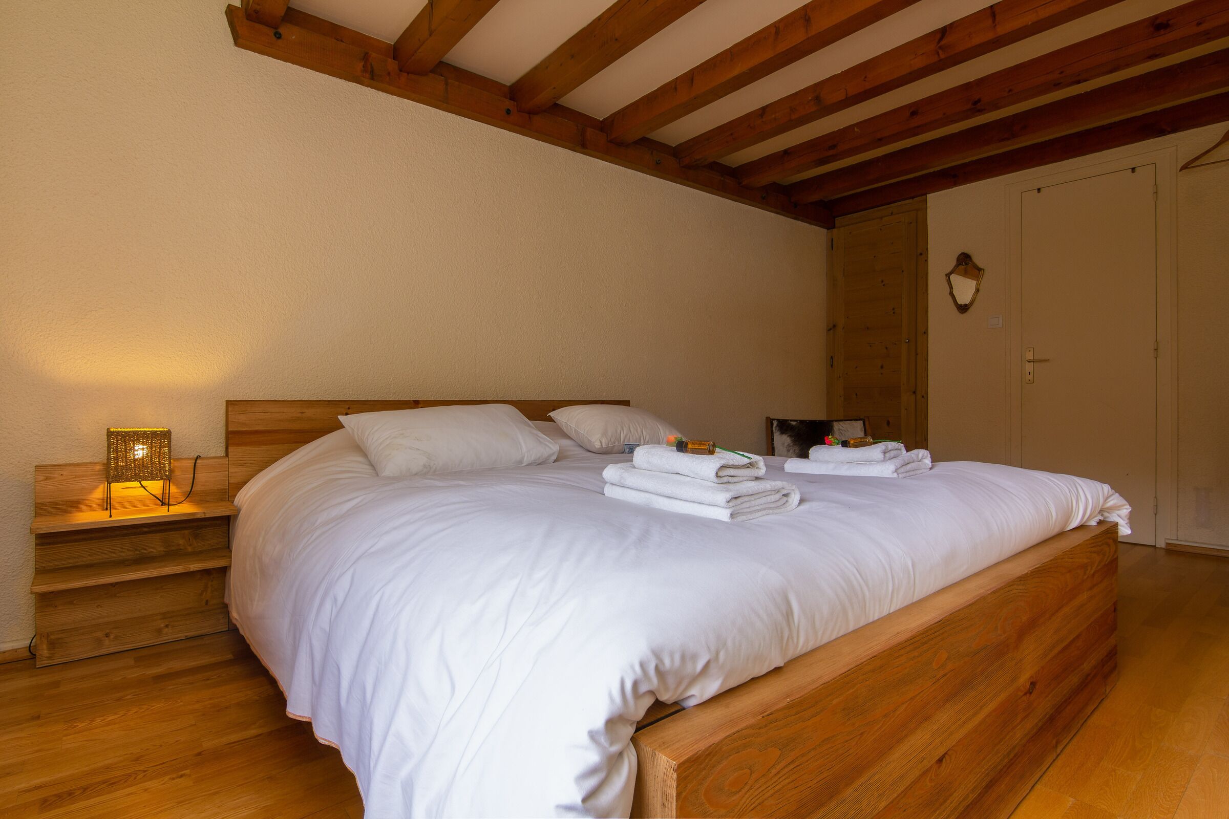Un lit bien fait, avec du linge de lit blanc et une tête de lit en bois, une lampe de chevet et une table de chevet en bois avec une lampe.
