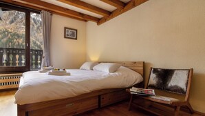 Una cama de madera con cabecera, una mesita de noche con una revista y una ventana con vistas a árboles.