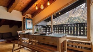 Una mesa de madera para comer con un banco, un sofá y un ventanal con vistas a la montaña.