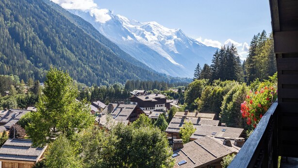 Un pueblo de montaña con casas de madera tradicionales, cielo despejado y picos nevados al fondo.
