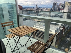 A balcony with a wooden table and chairs, overlooking a cityscape with modern buildings and a stadium. - Orange Stay Premier (Docklands)