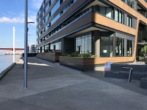 A modern building with a glass facade, a waterfront view, and a sign indicating a restaurant. - Orange Stay Premier (Docklands)