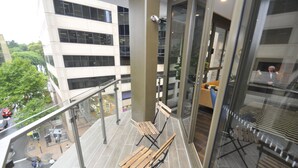 Un bâtiment moderne doté d’une façade en verre, d’un espace extérieur aménagé avec des bancs en bois et offrant une vue sur le paysage urbain.
