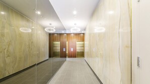 Un couloir moderne aux murs recouverts de marbre, doté d’un sol carrelé et de deux ascenseurs.