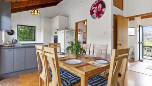 Comedor con mesa de madera, sillas y una planta en maceta. Se ve follaje verde por la ventana.