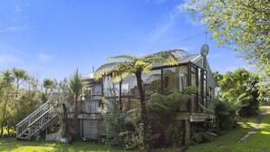 Una casa moderna con fachada de vidrio, rodeada de exuberante vegetación y una terraza de madera.