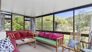 Una habitación iluminada por el sol con un sofá rojo, un sofá verde y una silla de madera.