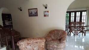 Ein Wohnzimmer mit einer Couch und einem Sessel, ein Essbereich mit Holzsesseln und eine Treppe.