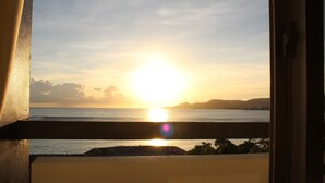 A sunset view from a balcony with a railing, overlooking a body of water and distant landforms.